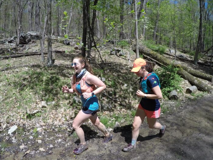 two women running on a trail through the woods