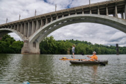 lady on a standup paddle board and a man in a kayak under a suspension bridge