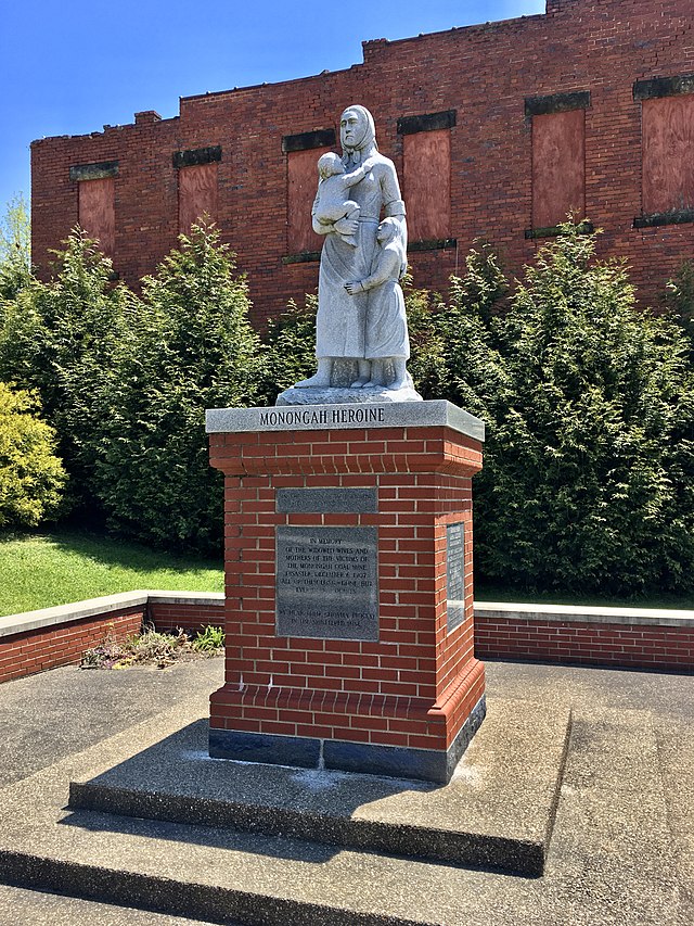 A white life size statue of a widowed mother and children siting on a brick base