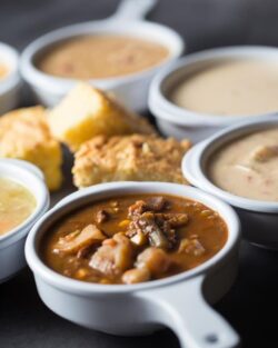 bowls of various soups with biscuits and cornbread in the middle
