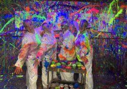four women dressed in white overall splattered with paint